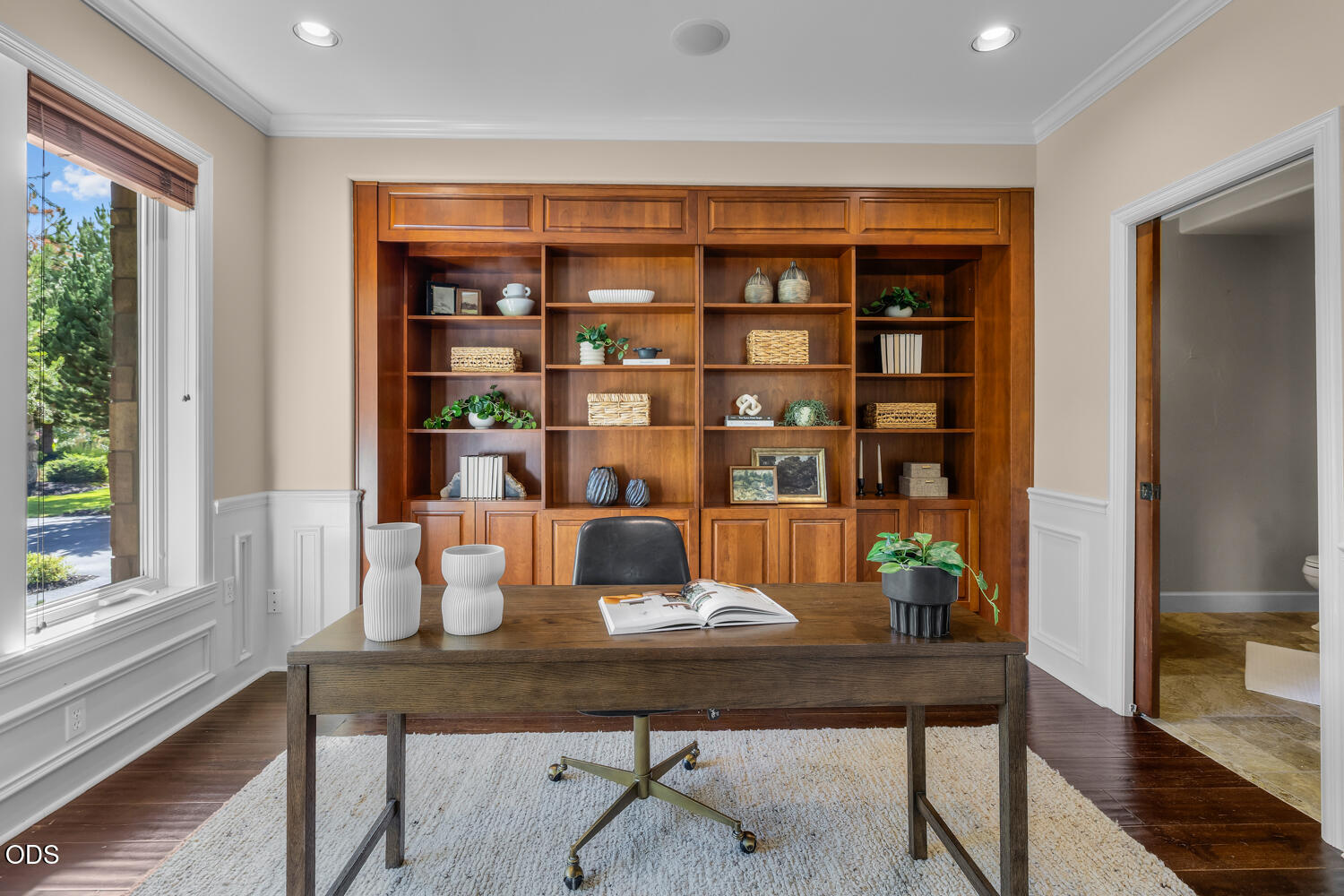 Home office with built-in wood bookshelves, a dark desk, and a large window overlooking greenery.