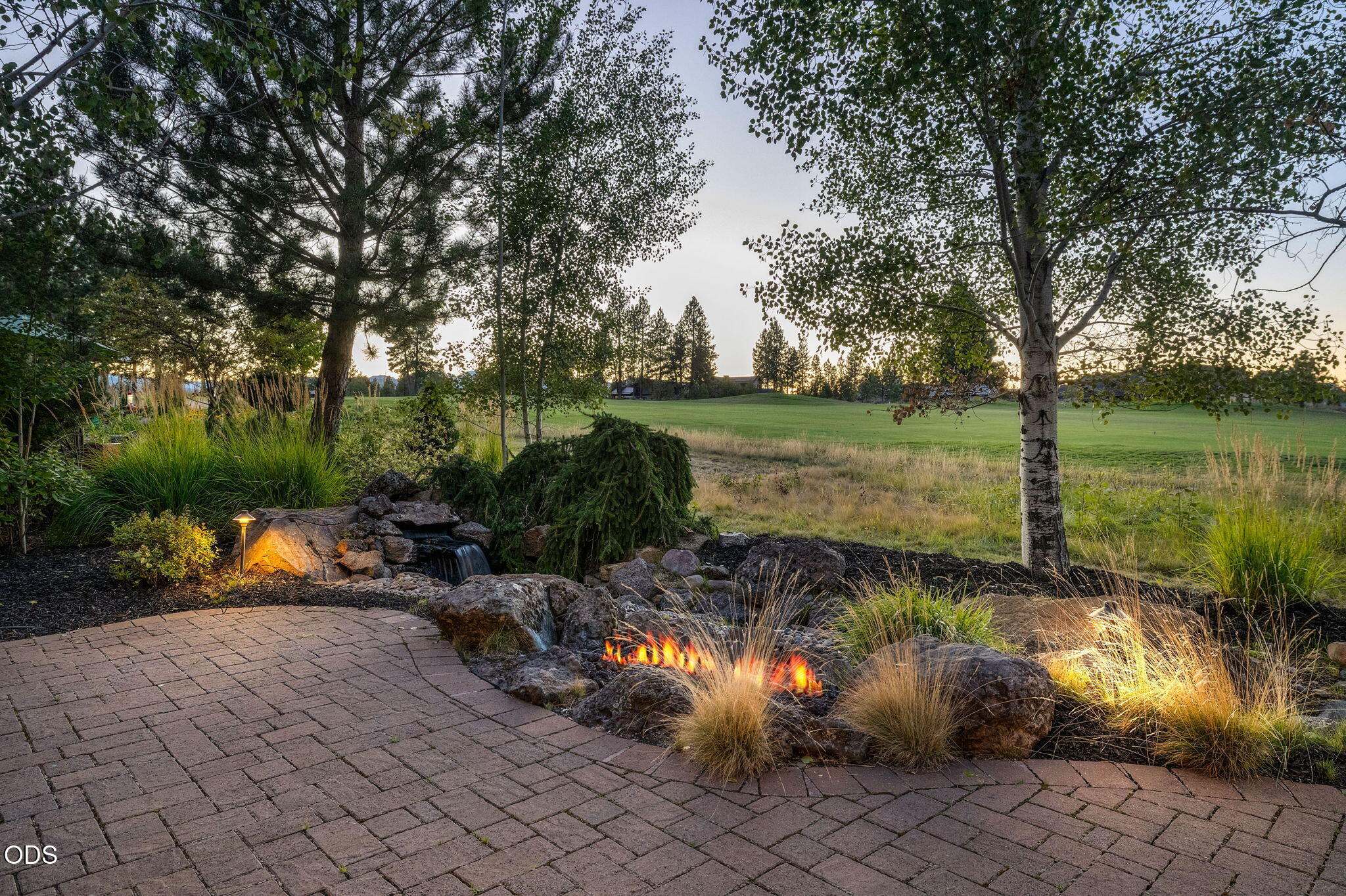 Landscaped patio with a rock water feature and small fire feature beside an open grassy area.