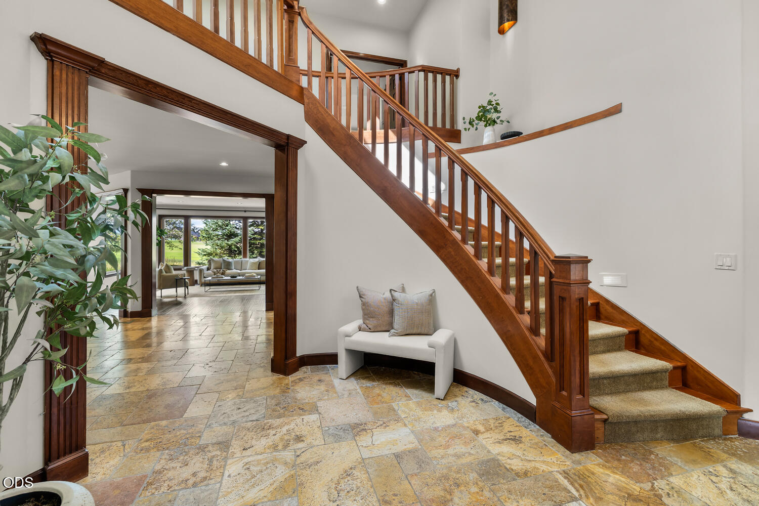 Foyer with sweeping wood staircase, stone tile floors, and a view into the furnished living room.