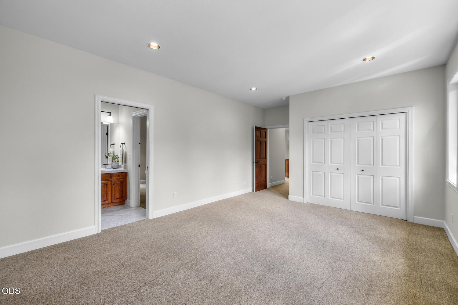 Empty carpeted bedroom with a large double-door closet and an adjoining bathroom doorway.