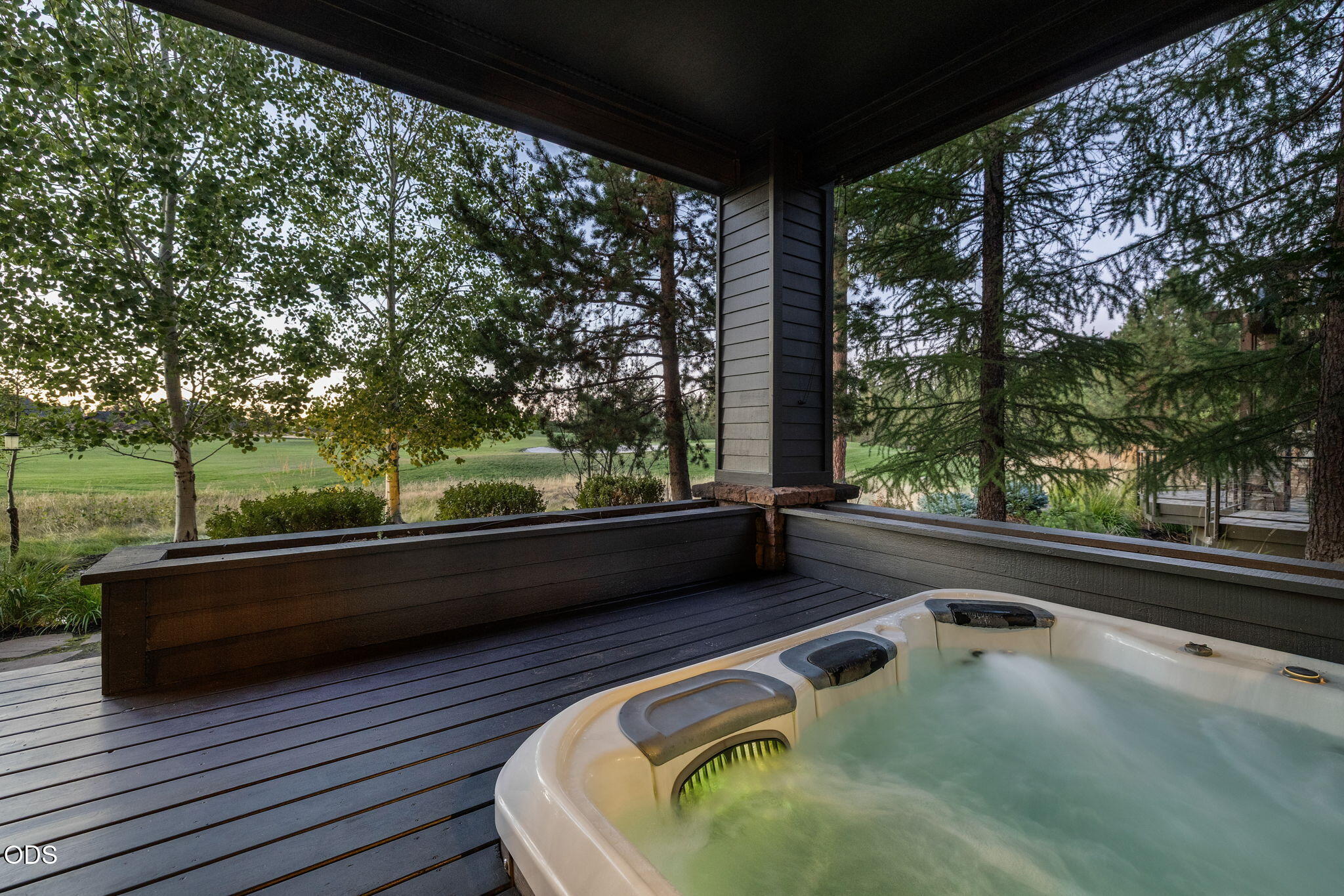 Covered deck hot tub overlooking a green golf course through trees.