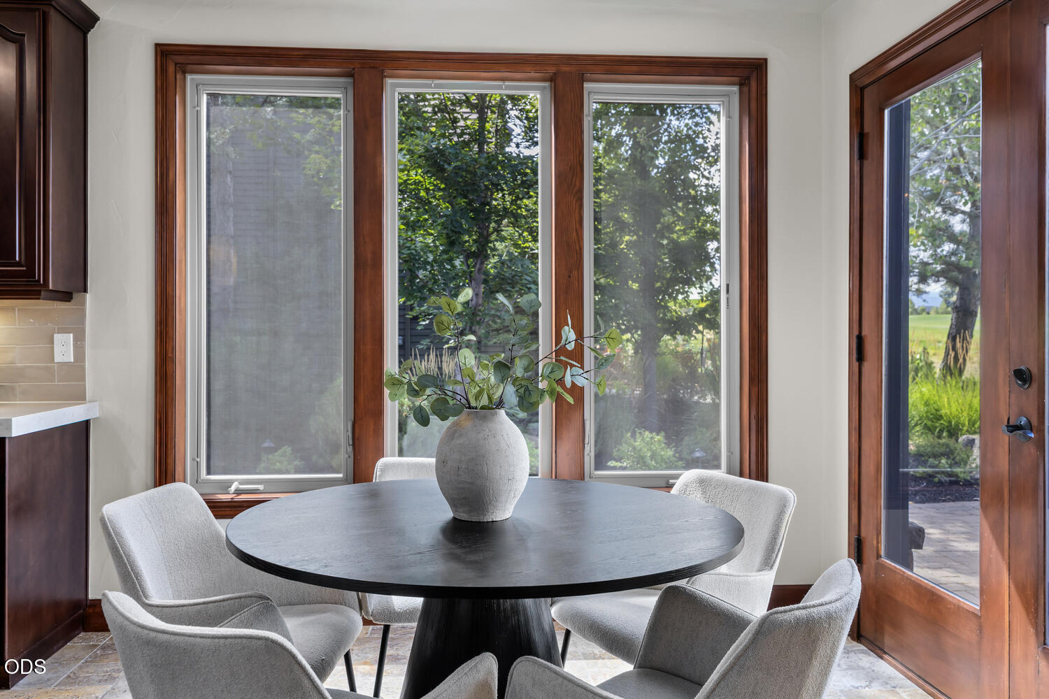Dining area with a round dark table, light chairs, large windows, and a glass patio door.