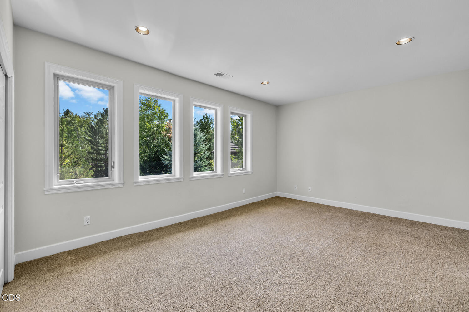 Unfurnished carpeted room with four windows overlooking trees.