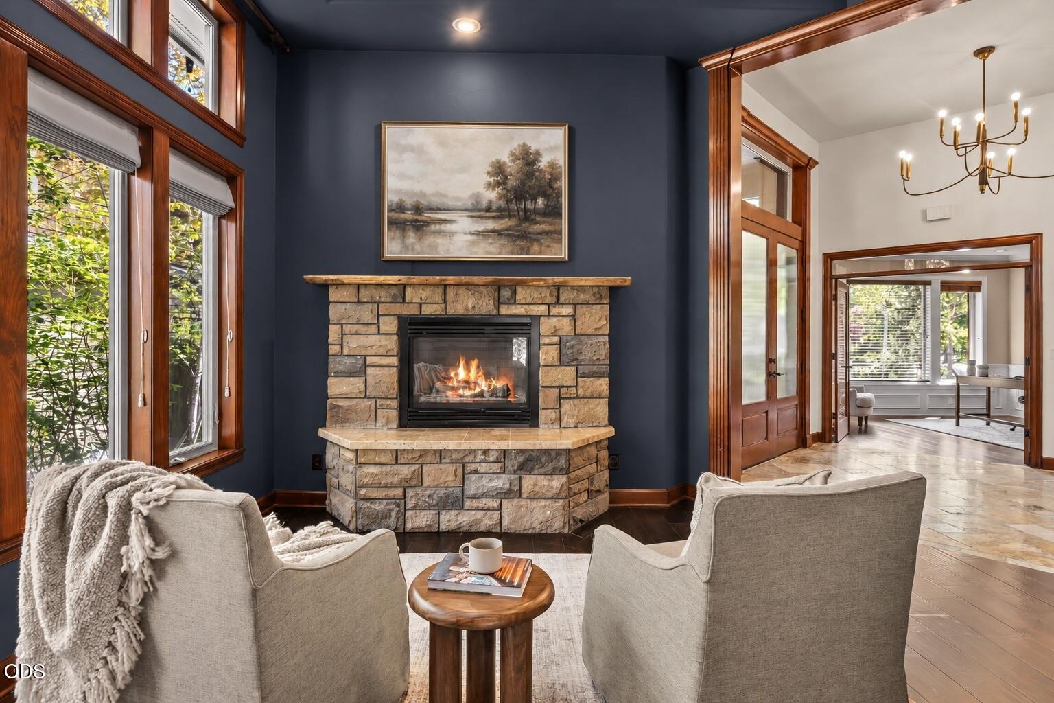 Living room with a stone fireplace, dark blue walls, tall windows, and wood trim.
