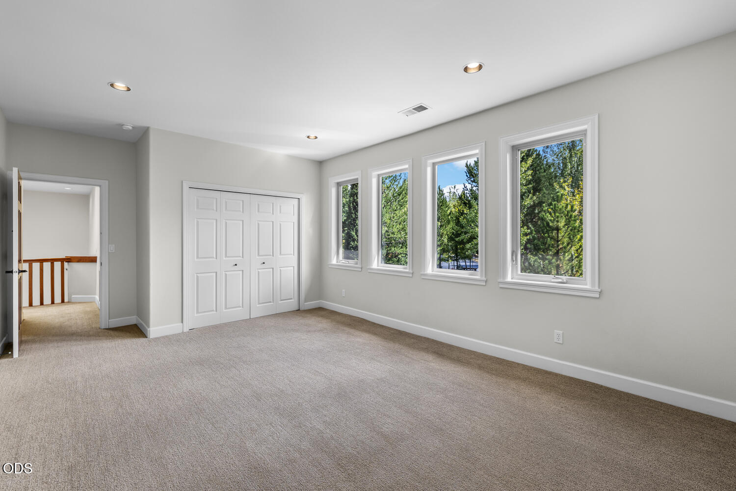 Empty carpeted bedroom with a wide closet and tall windows overlooking trees.