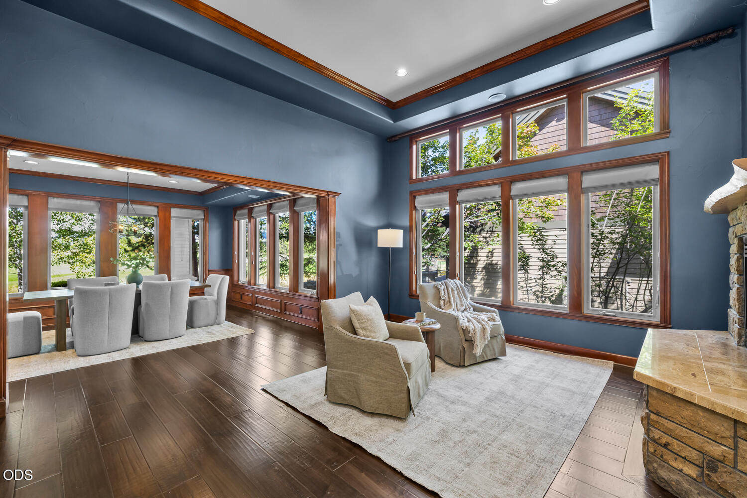 Living room with tall windows, blue walls, wood trim, and two armchairs beside a stone fireplace.