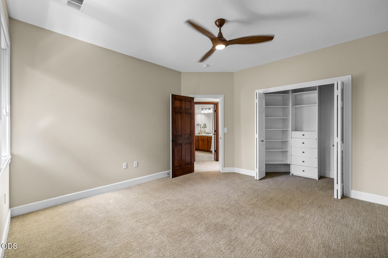 Unfurnished bedroom with a built-in closet, carpet, ceiling fan, and open doorway to a bathroom.