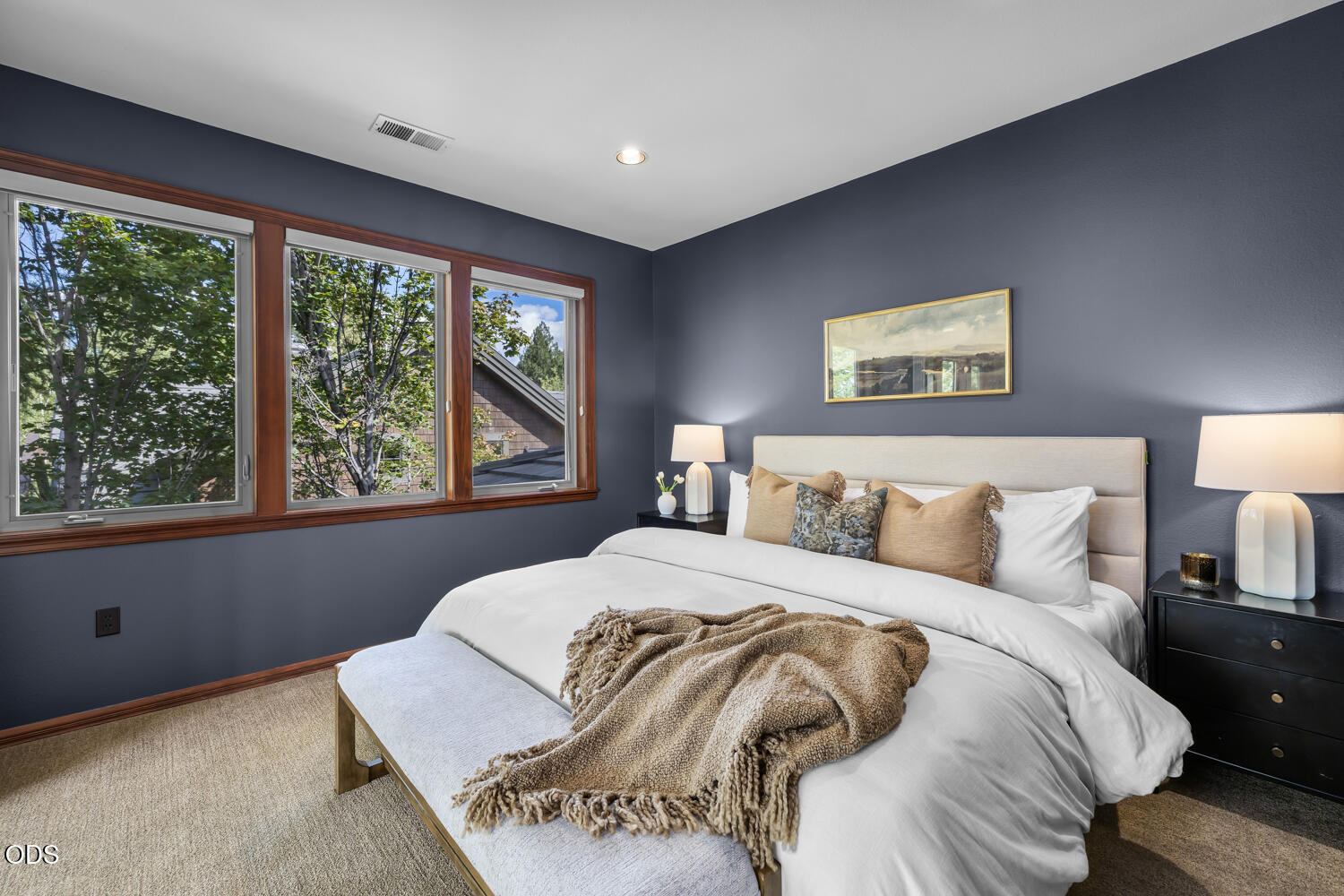Staged bedroom with a white bed, dark blue walls, and wide wood-trimmed windows.
