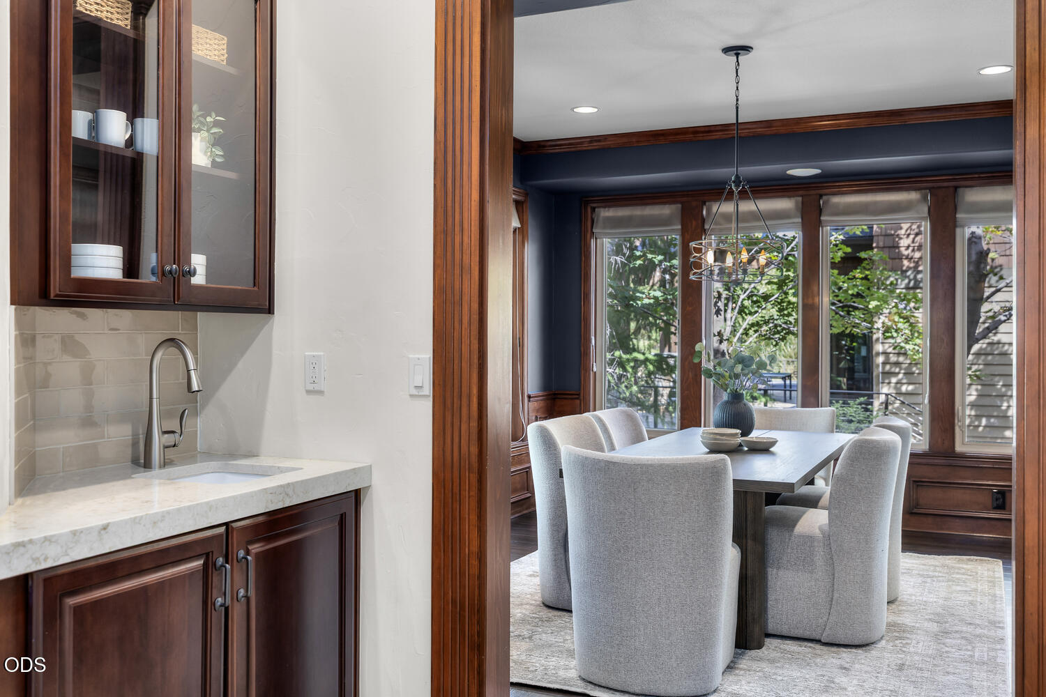 Dining room with large windows, upholstered chairs, and an adjoining built-in wet bar.