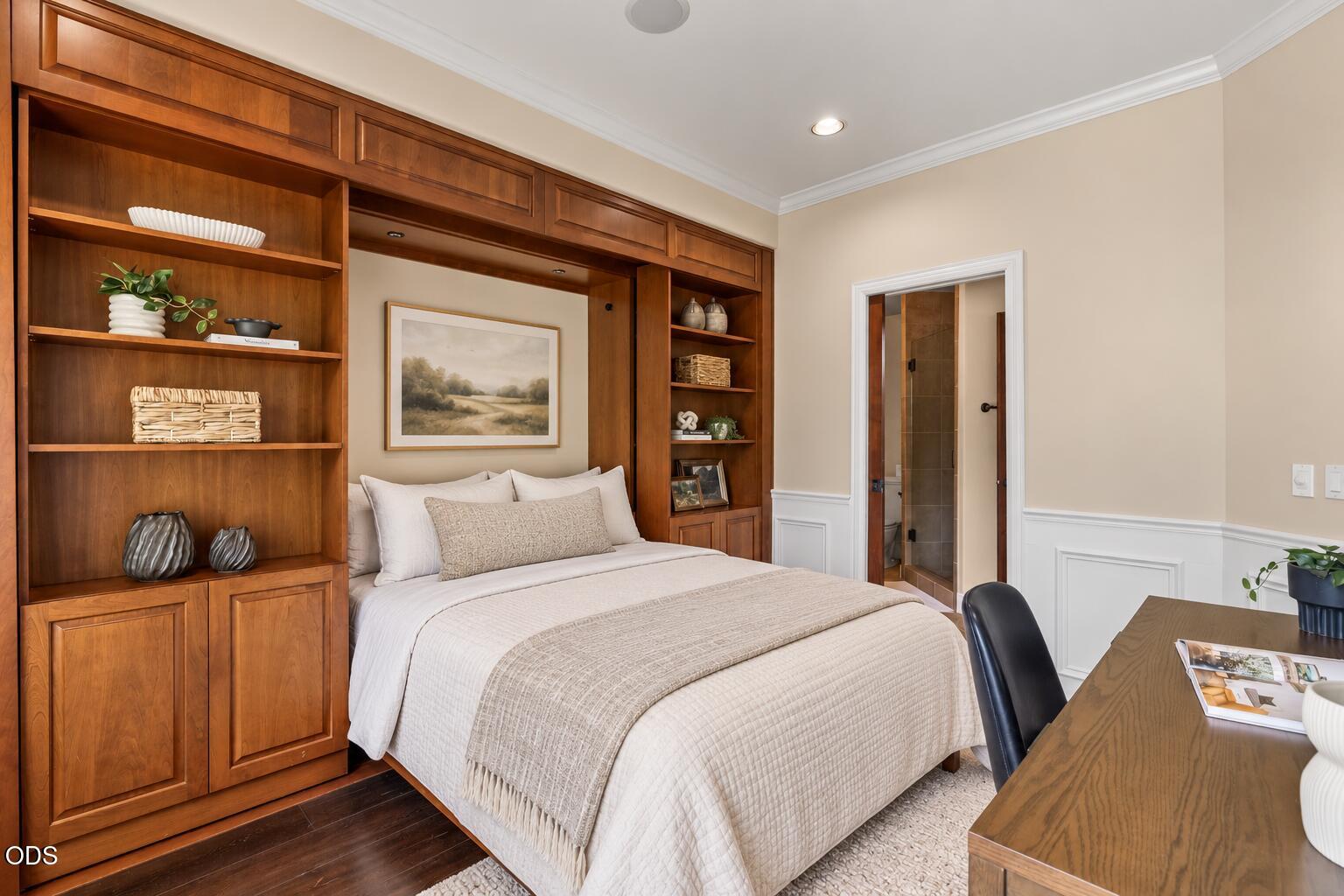 Bedroom with a bed framed by built-in wood cabinetry and shelves, with a tiled bathroom doorway nearby.