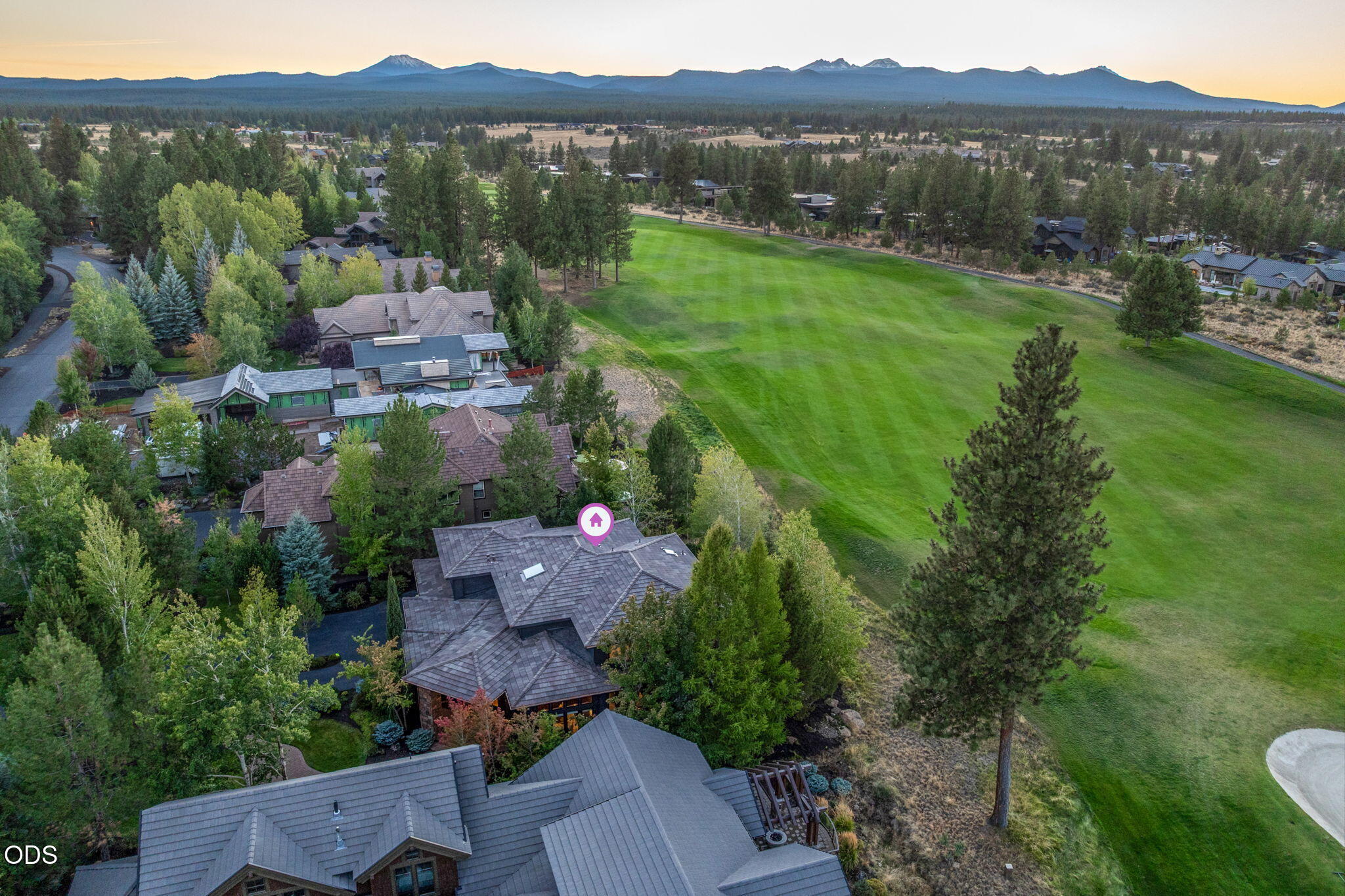 Aerial view of a tree-surrounded home beside a golf course, with mountains in the distance.