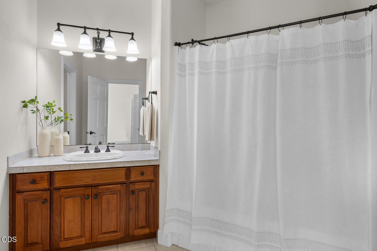 Bathroom with a warm wood vanity, white countertop, large mirror, and white shower curtain.