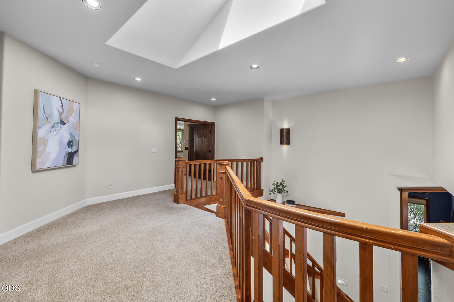 Carpeted upstairs landing with a wooden railing around the stairwell and a large skylight.