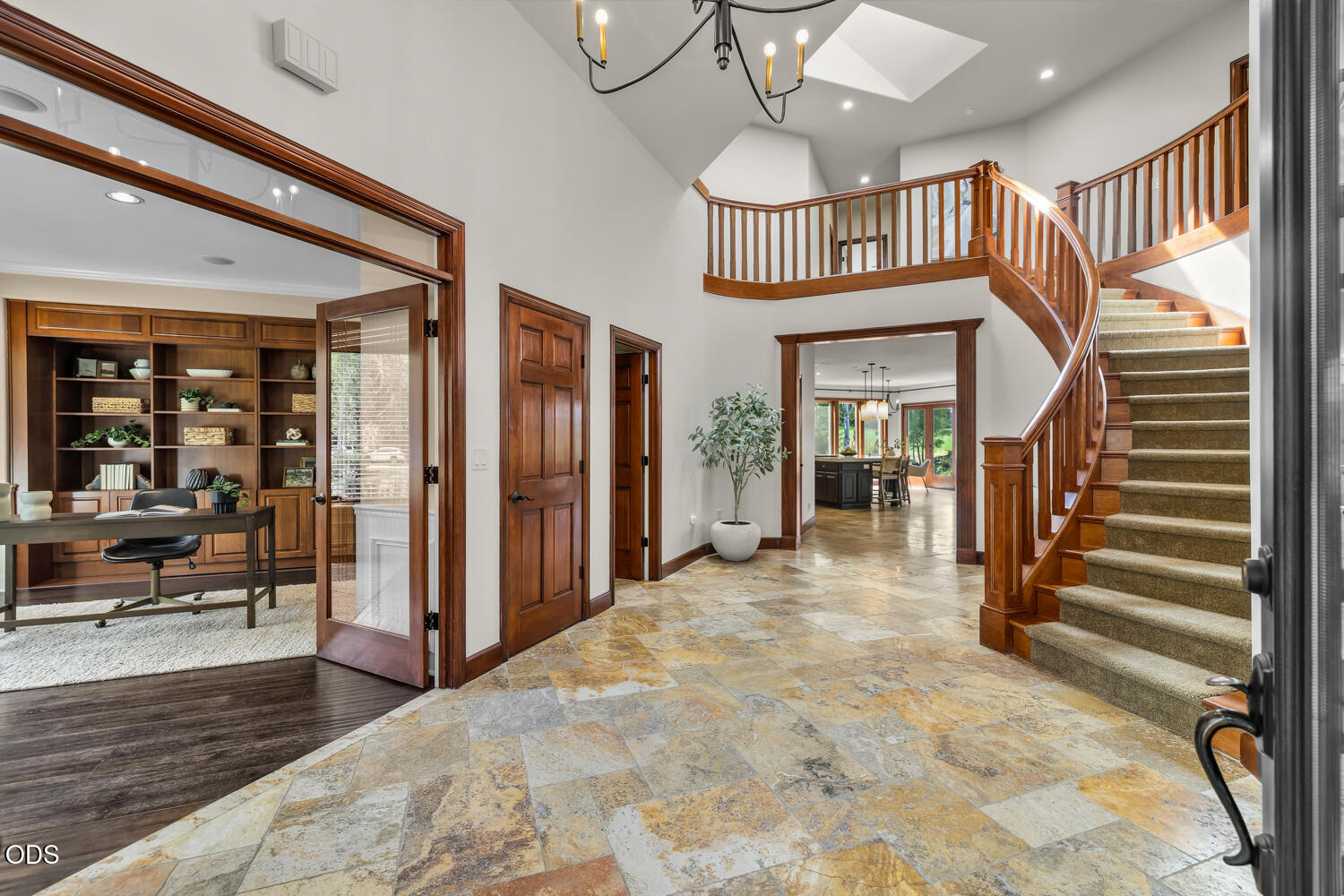 Entry foyer with a curved wood staircase, stone tile floor, and adjoining office with built-in shelving.