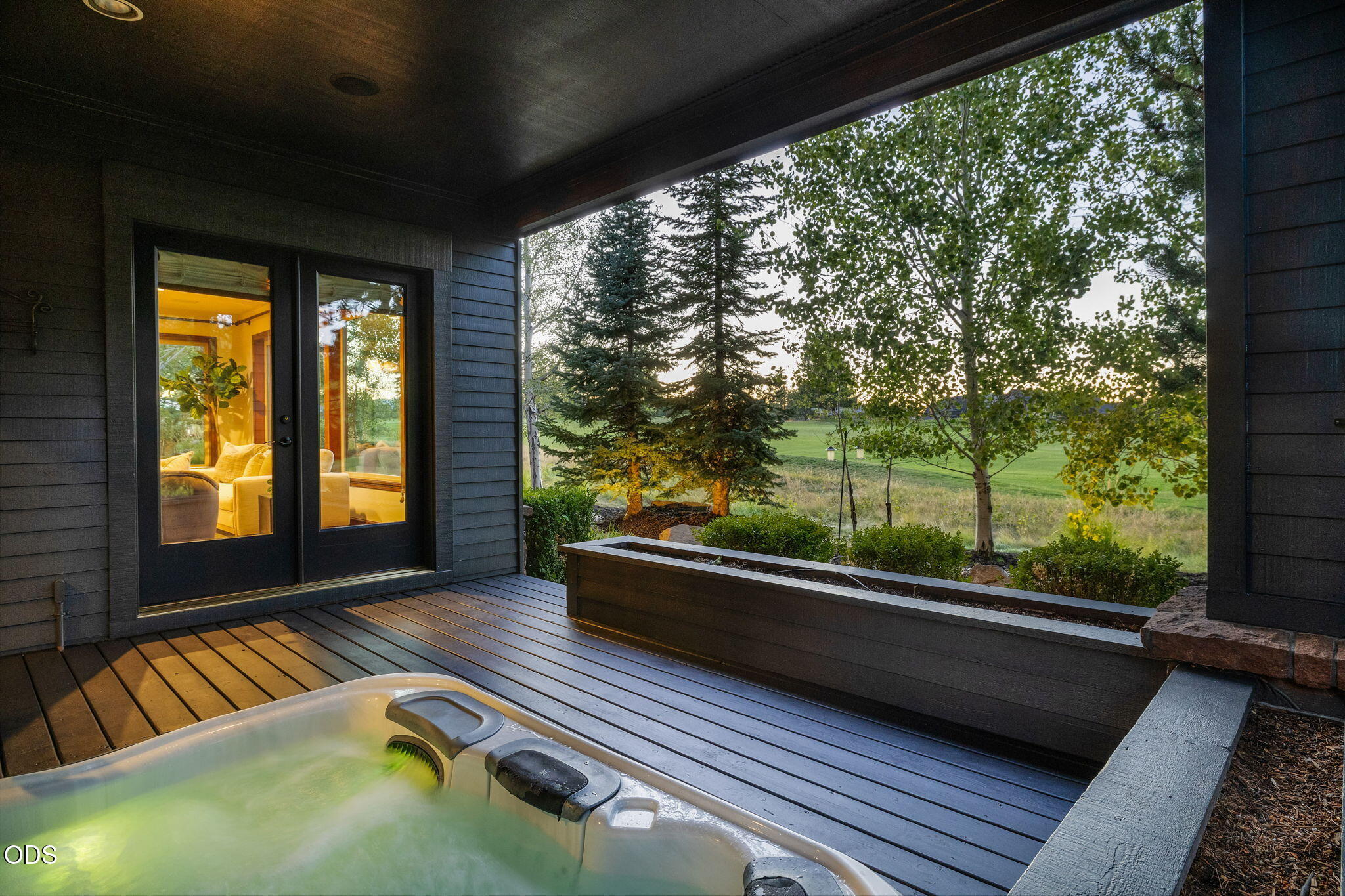 Covered deck hot tub overlooking trees and a manicured green lawn.