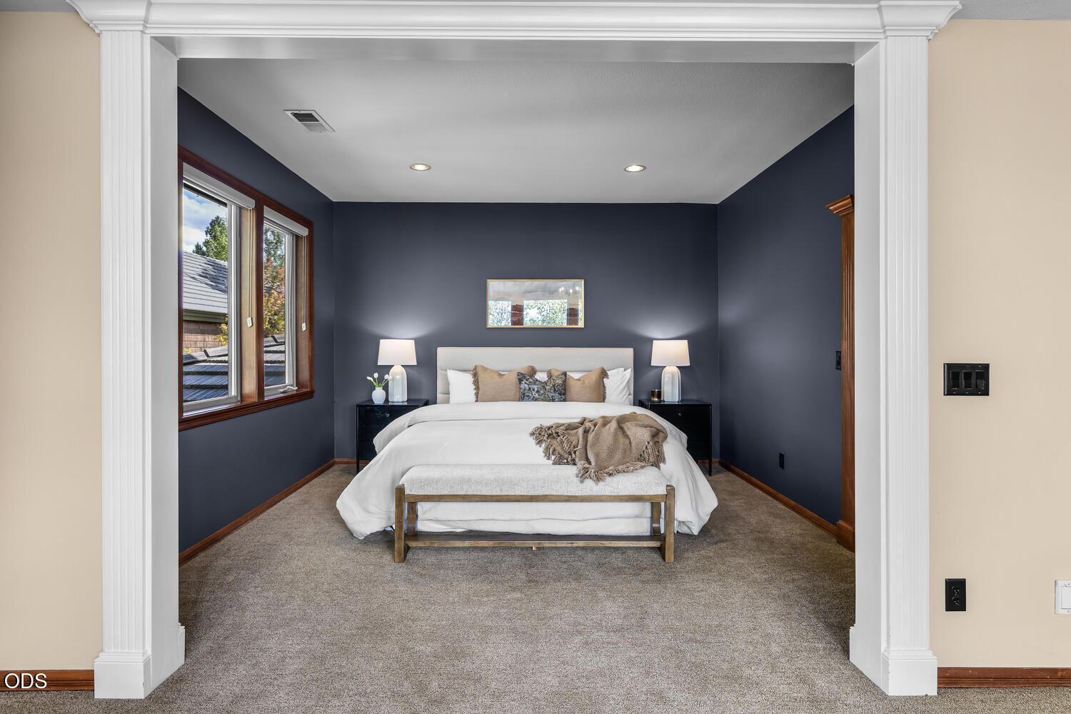 Bedroom with a white bed against navy walls and wood-trimmed windows.