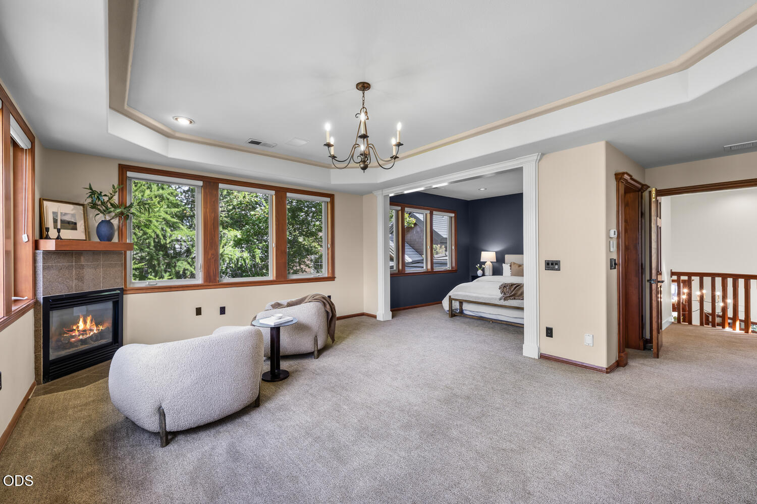 Living room with a lit fireplace, large windows, and an adjoining bedroom.