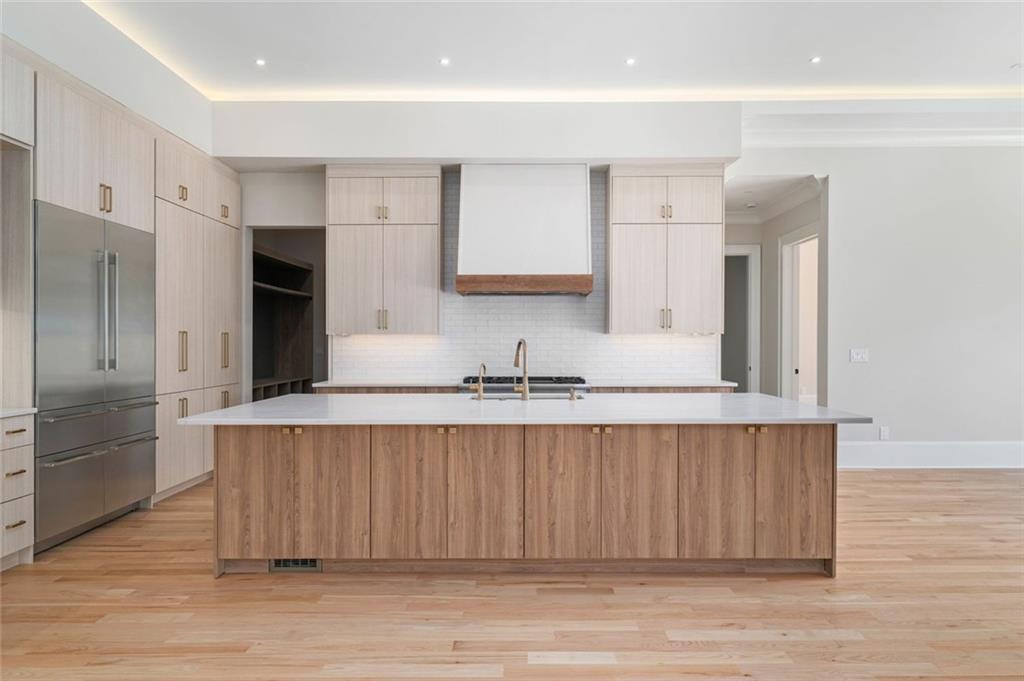 Modern kitchen with a large wood-front island, stainless steel appliances, and light wood floors.