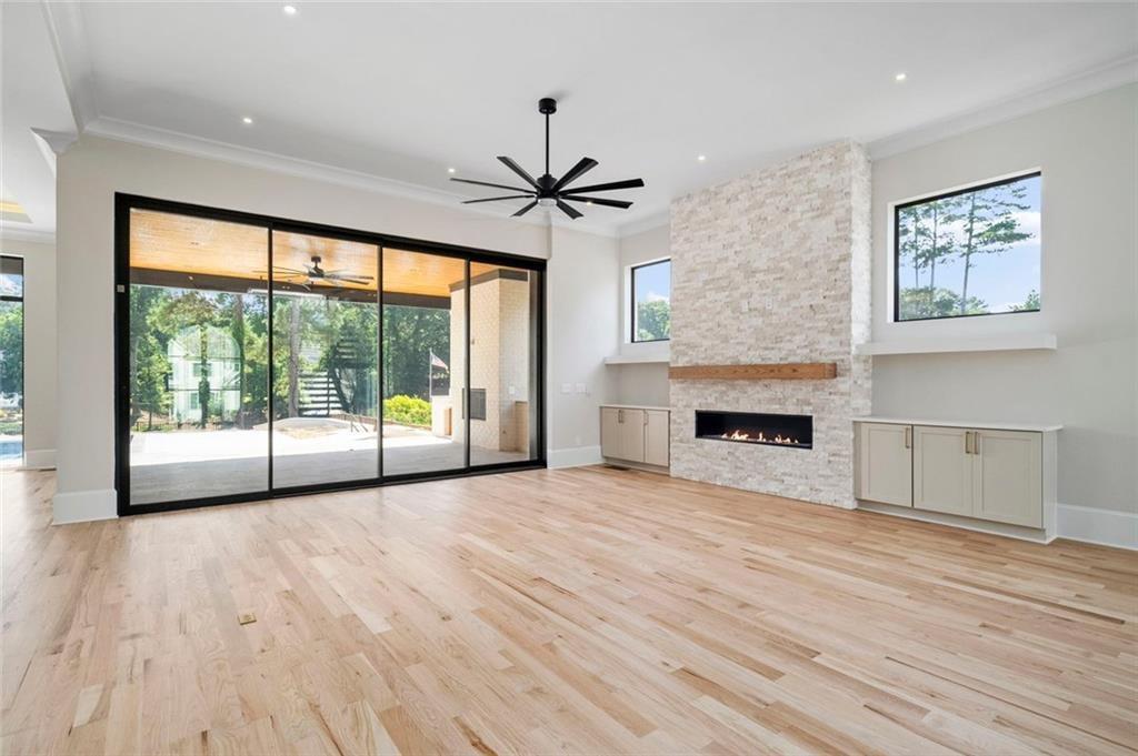 Living room with a stone fireplace, pale wood floors, and wide sliding glass doors.