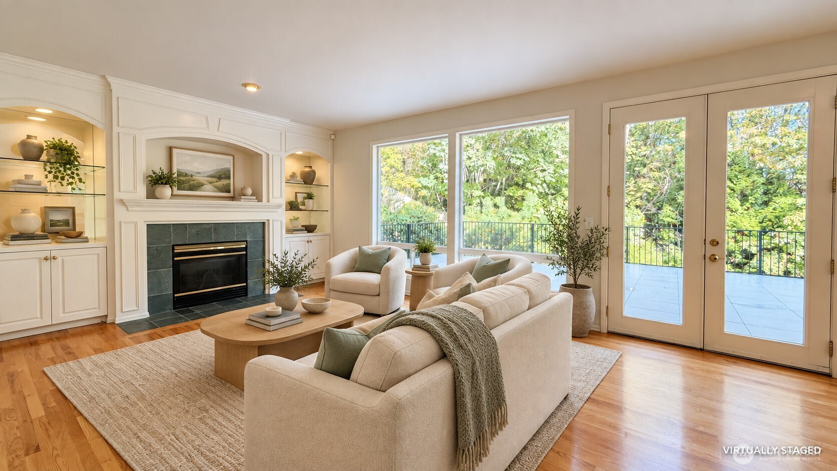 Living room with a tiled fireplace, cream seating, hardwood floors, and large windows overlooking greenery.