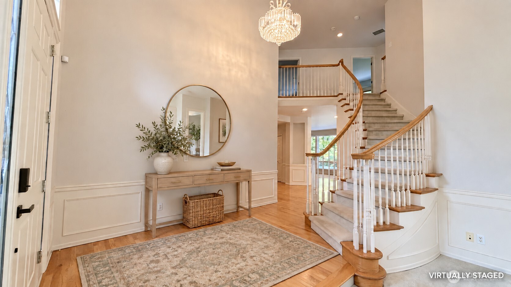 Two-story entry foyer with a curved staircase, chandelier, hardwood floors, and console table beneath a round mirror.