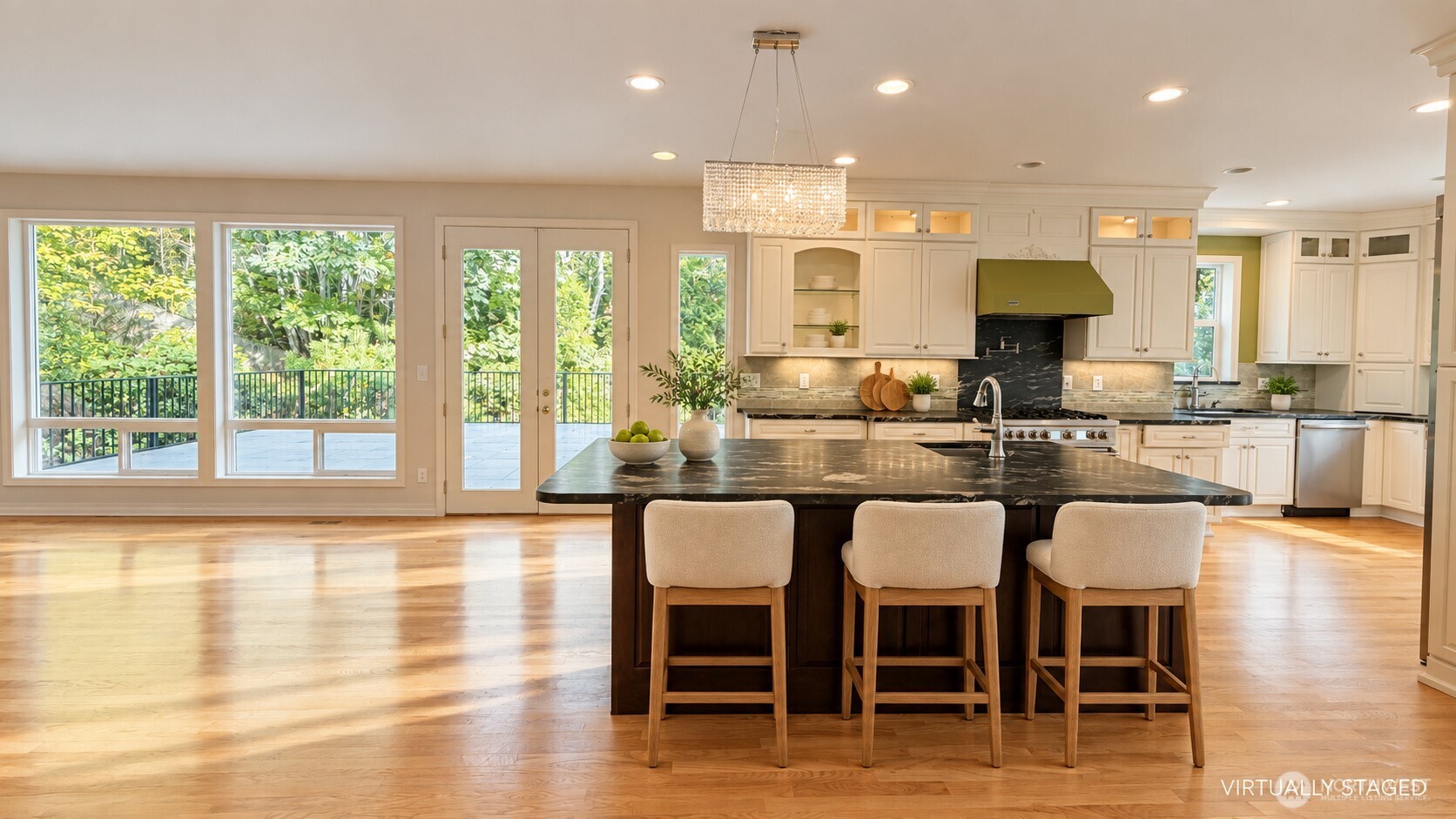 Kitchen with a large dark island, white cabinetry, and windows overlooking leafy greenery.