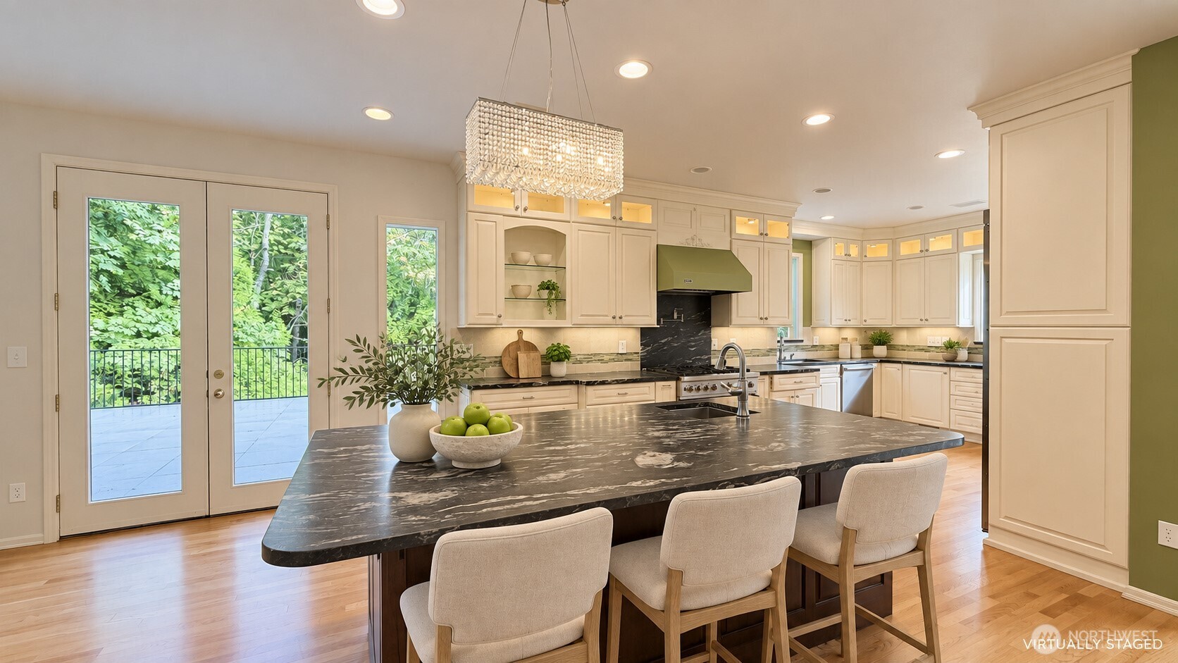 Kitchen with a dark veined island, cream cabinetry, crystal pendant, and glass doors overlooking greenery.