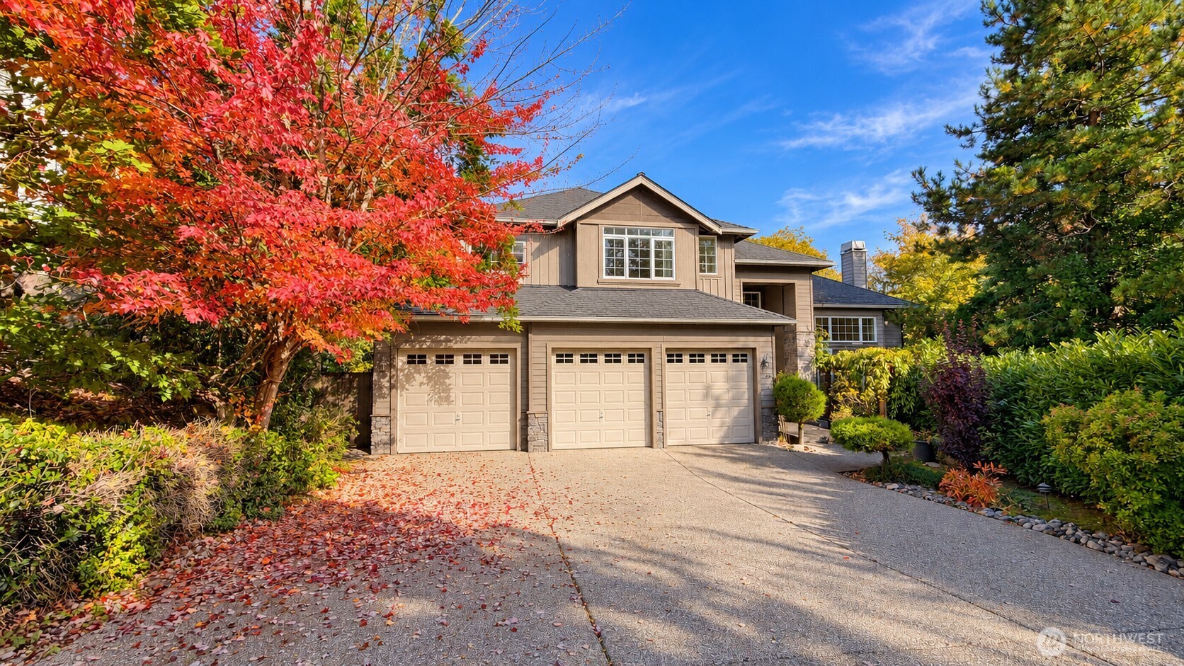 Two-story home with a three-car garage, framed by red autumn foliage and a landscaped driveway.