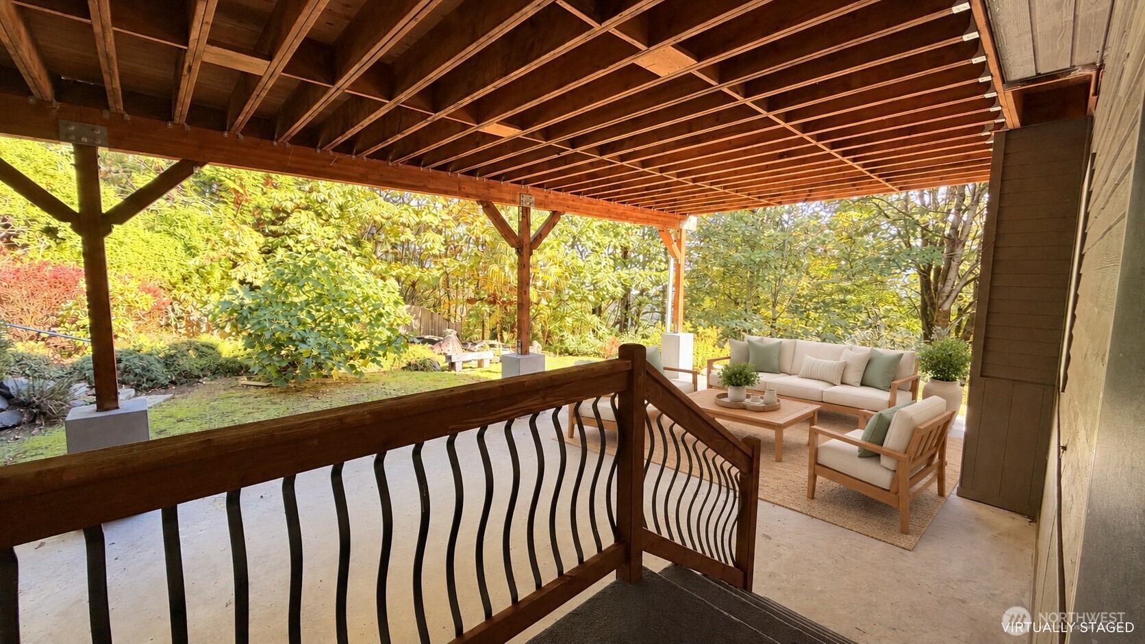 Covered patio with exposed wood rafters, dark railing, and staged seating overlooking a leafy garden.
