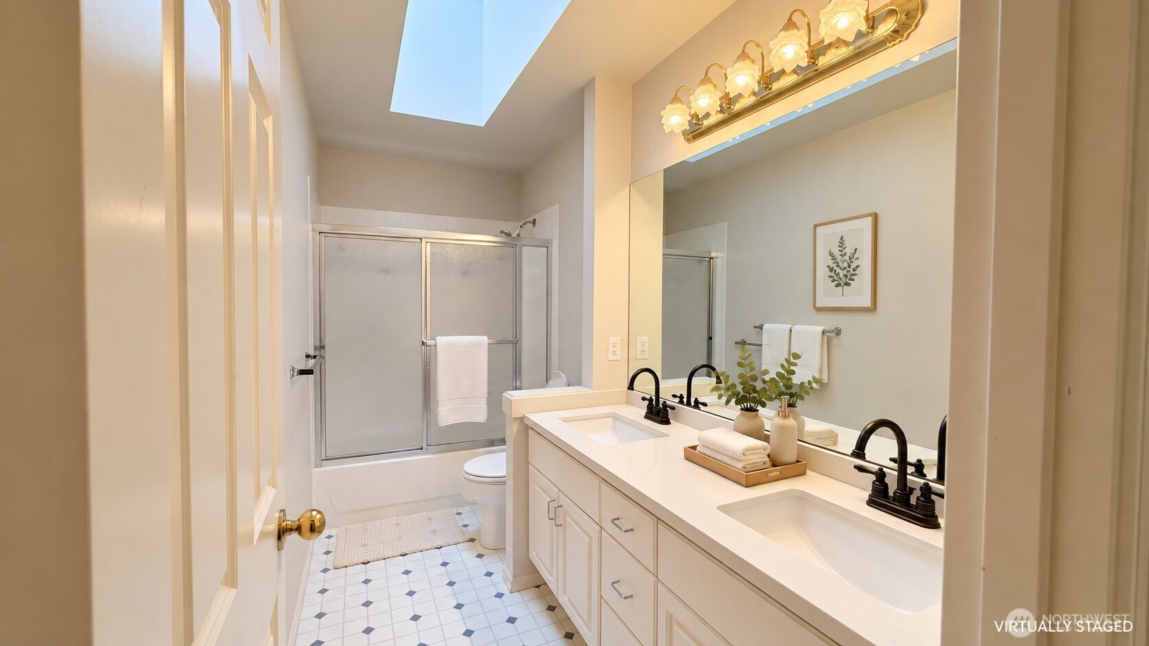 Bathroom with a double-sink vanity, glass-enclosed shower, patterned tile floor, and skylight.