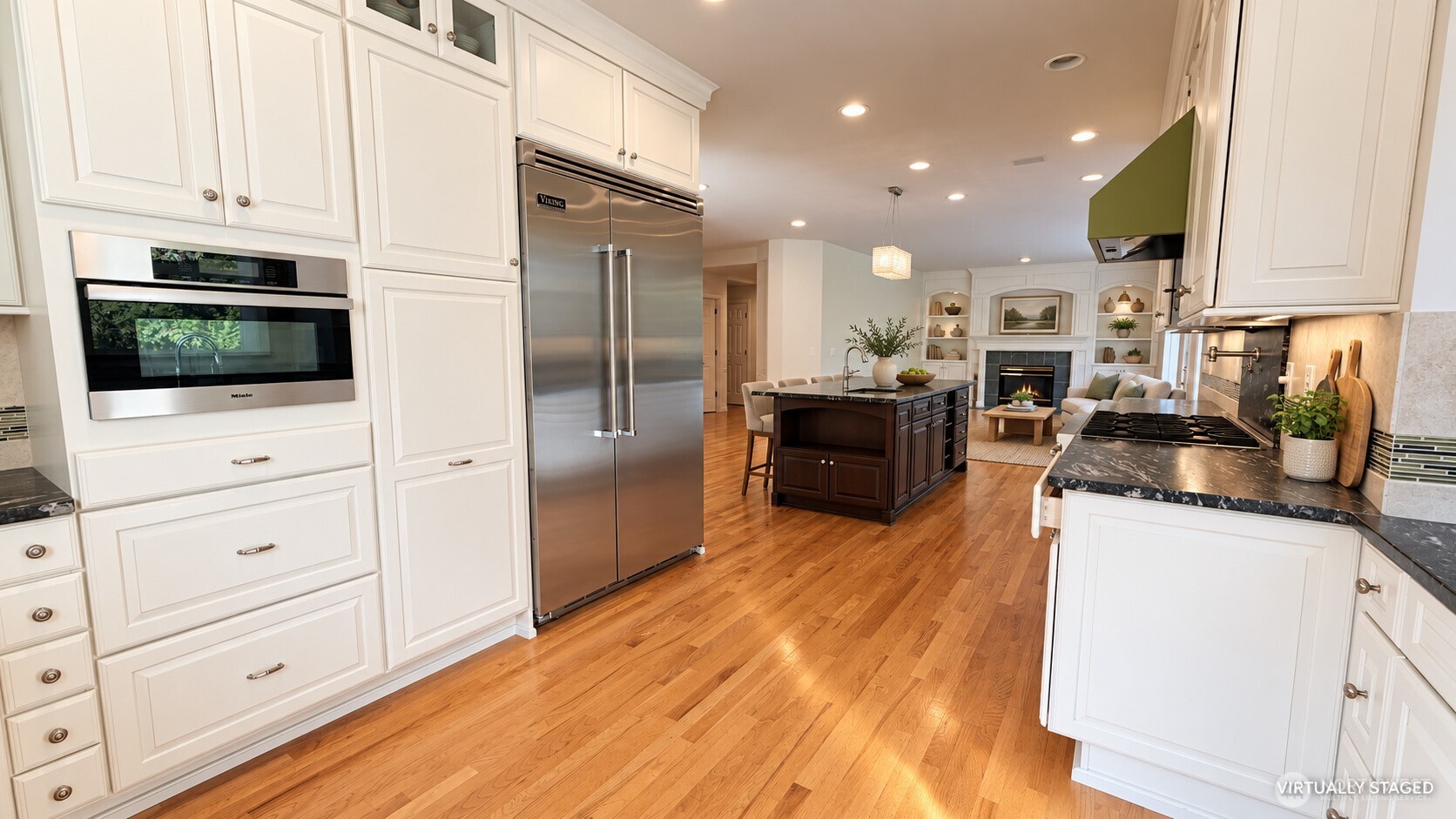 Kitchen with white cabinets, stainless appliances, hardwood floors, and a dark island opening to a living room.