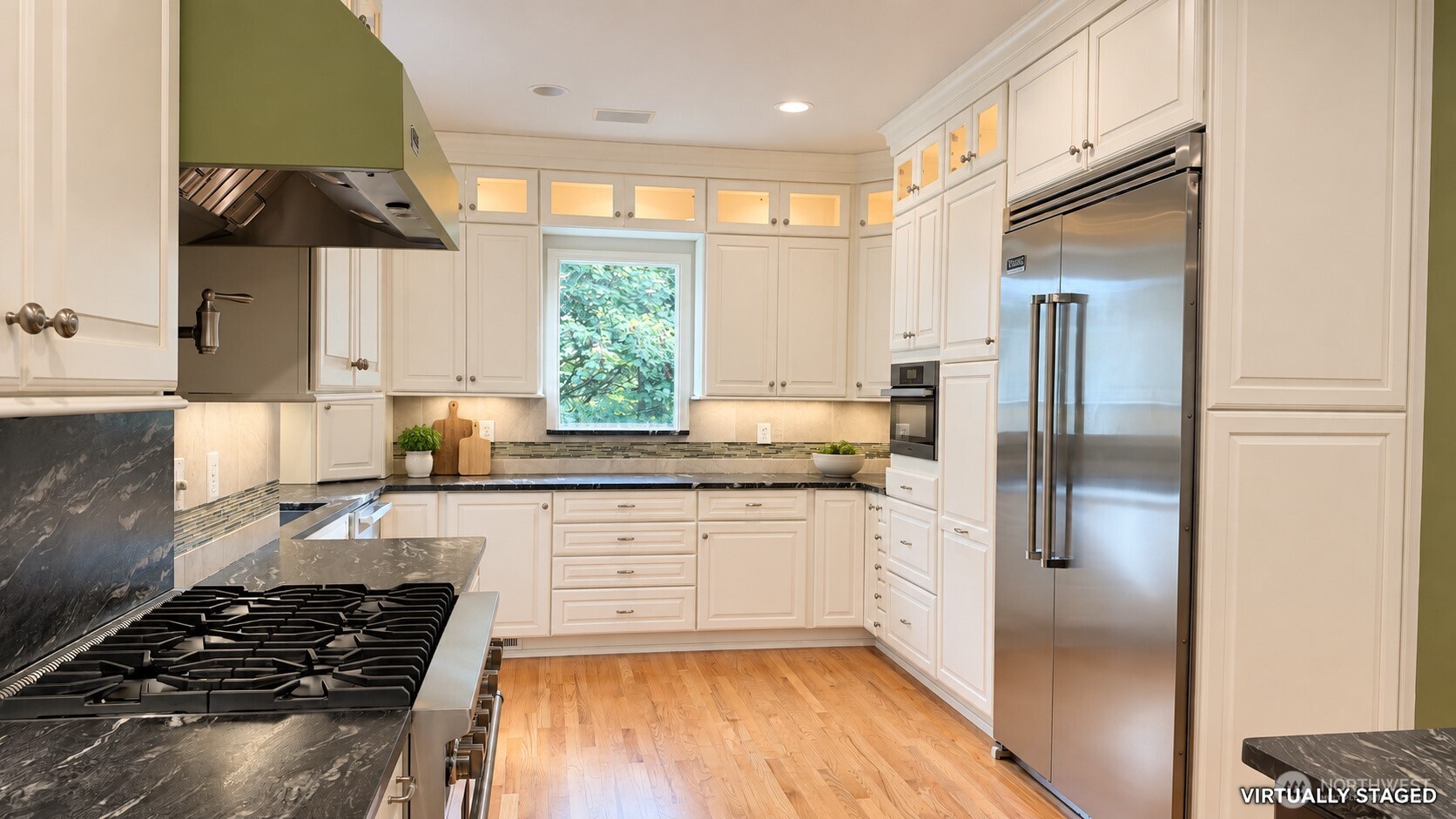 Kitchen with white cabinets, dark stone counters, stainless appliances, and hardwood floors.
