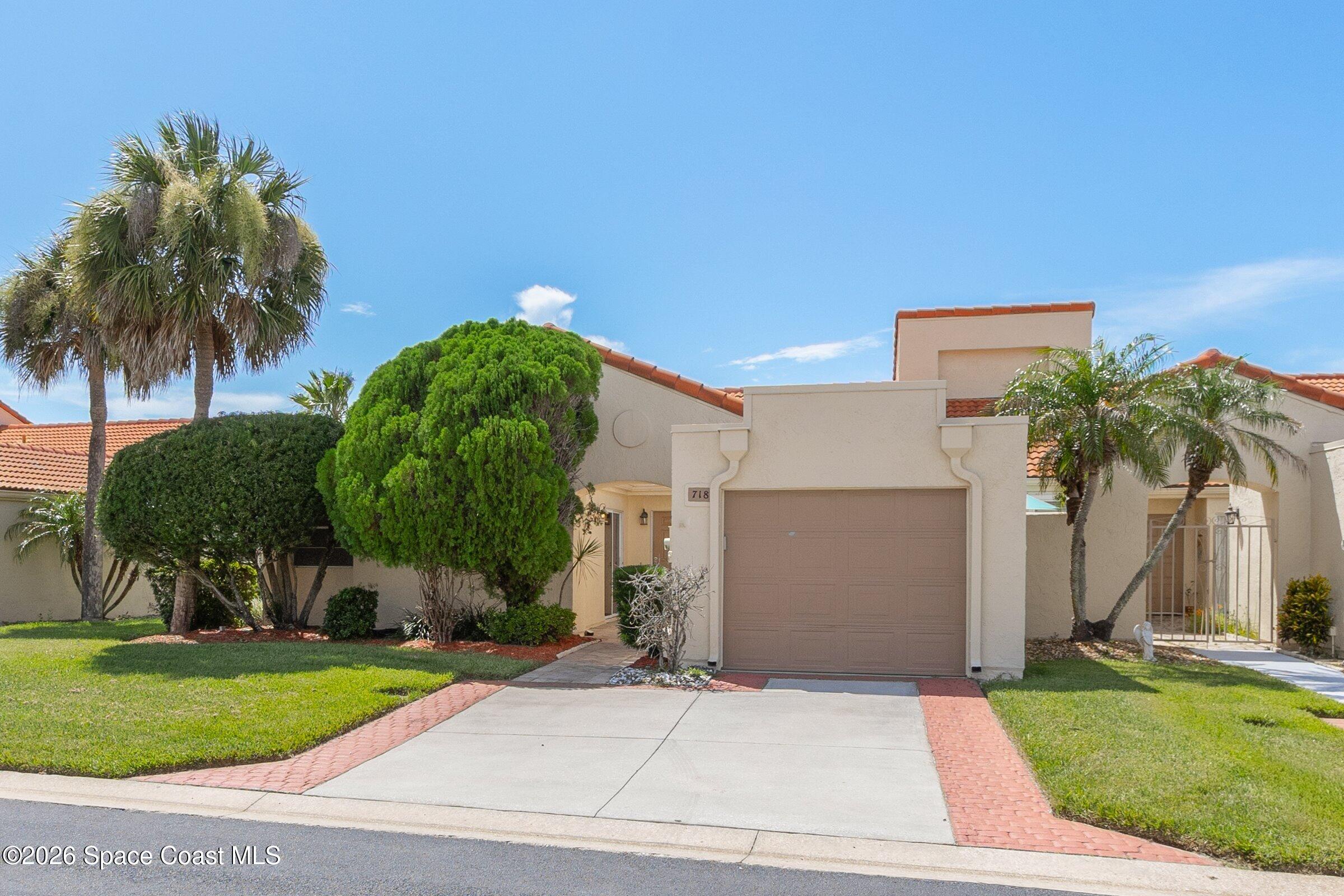 Beige stucco home with a terracotta tile roof, single garage, and landscaped lawn with palm trees.