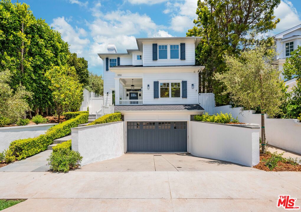 White two-story house with blue shutters, a covered entry, and a gray garage door.