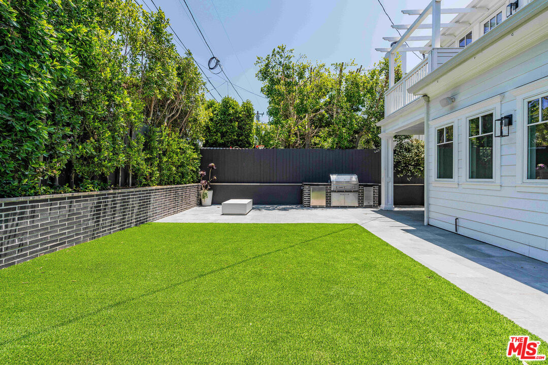 Backyard with a broad green lawn, paved patio, and built-in outdoor grill beside a white house.