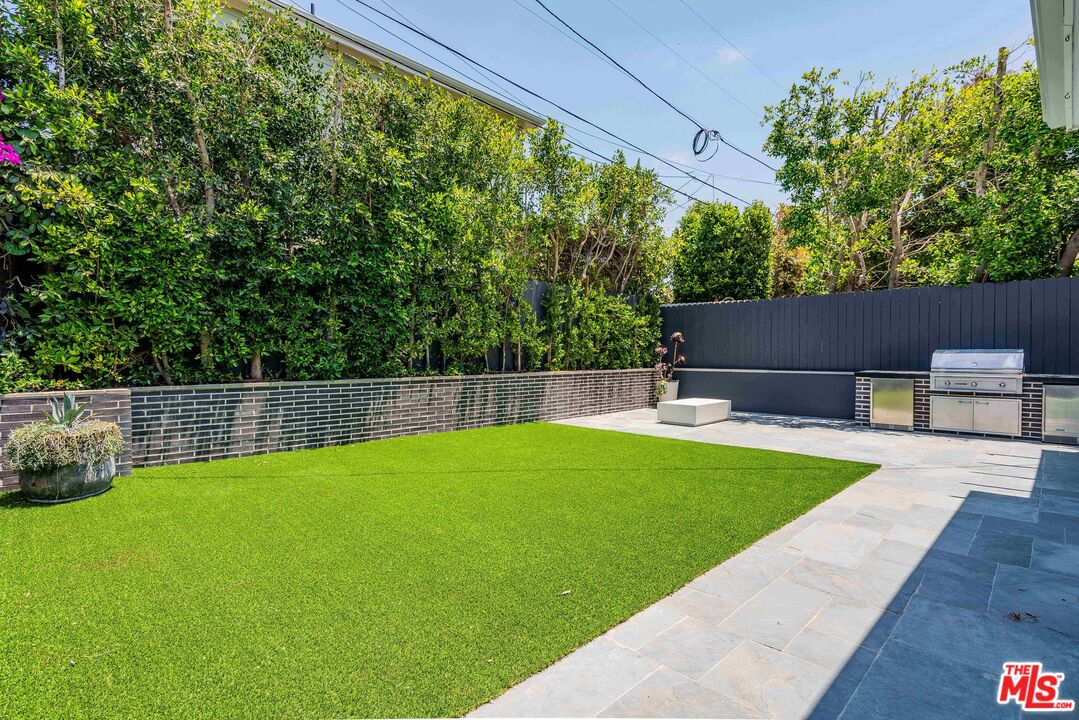 Backyard with a bright green lawn, stone patio, privacy hedges, and built-in outdoor kitchen.