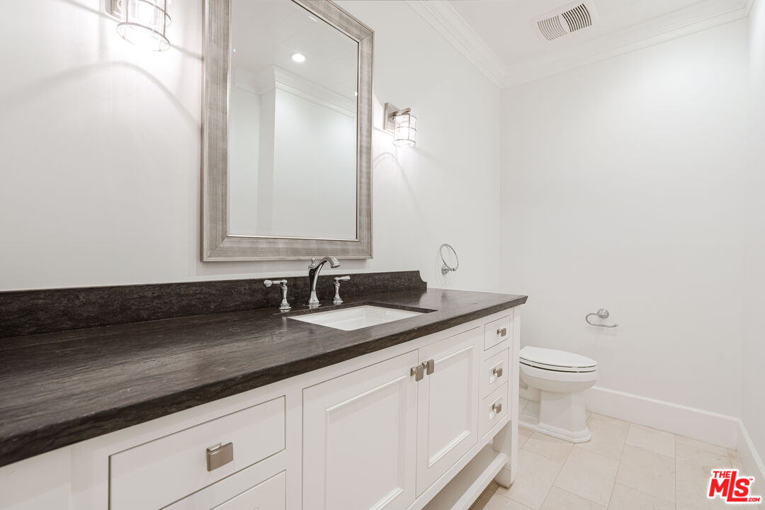 Bathroom with a dark stone vanity, white cabinetry, framed mirror, and toilet.