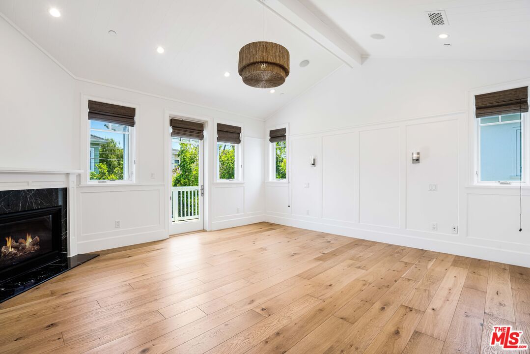 Unfurnished living room with wide-plank wood floors, a black marble fireplace, and windows opening to greenery.