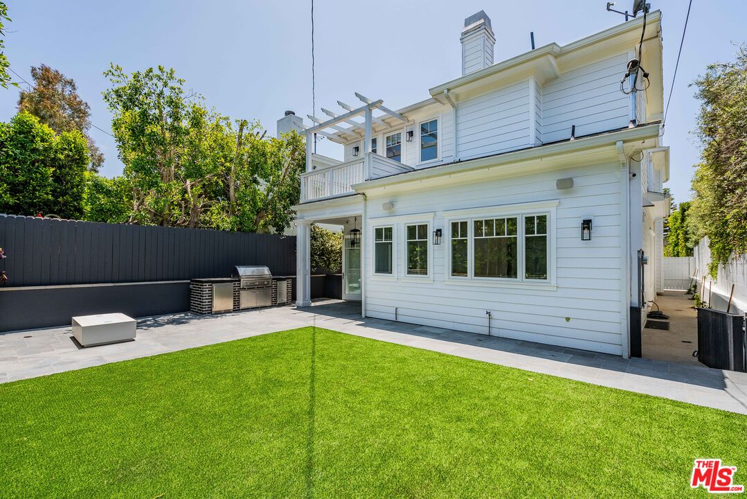 White two-story home overlooking a green lawn and paved backyard patio with an outdoor grill.