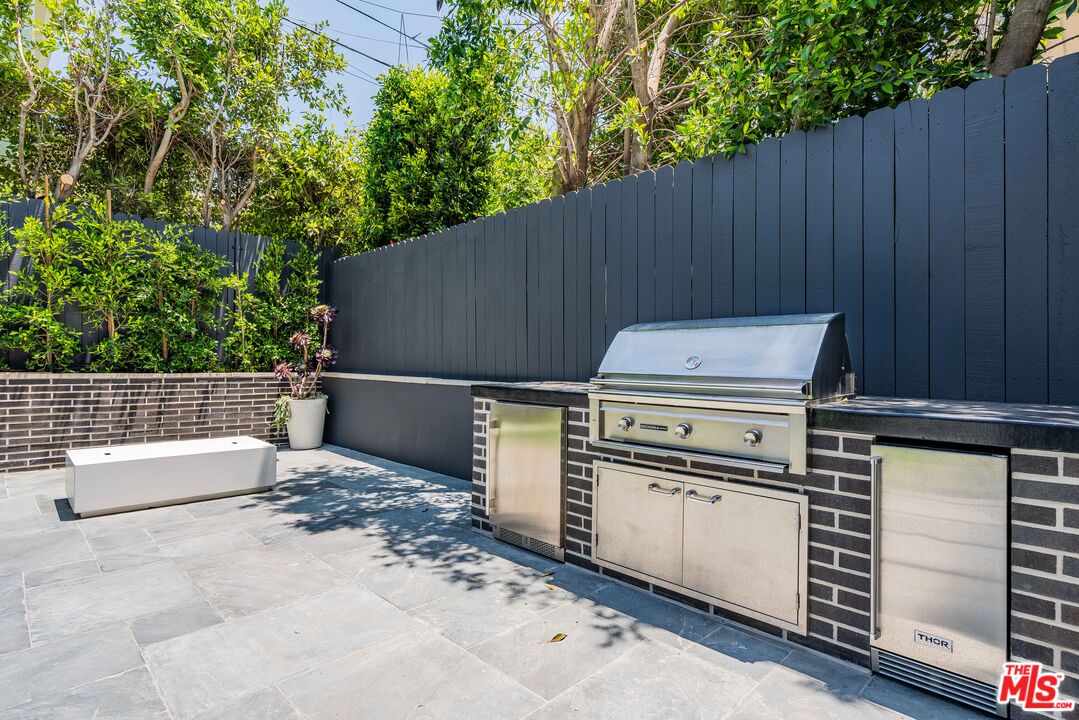 Outdoor patio with a built-in stainless steel grill, dark brick counter, and tall privacy fence.