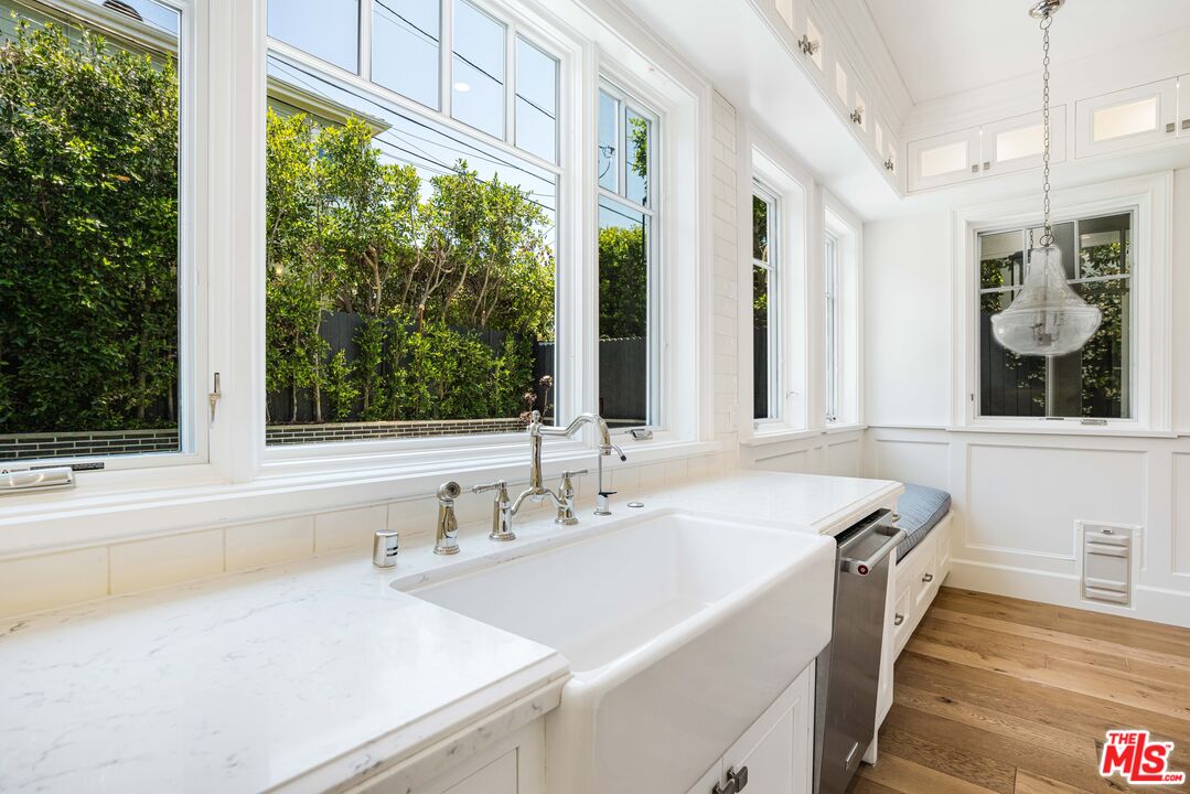 Bright white kitchen with farmhouse sink, wide garden-facing windows, and hardwood floors.