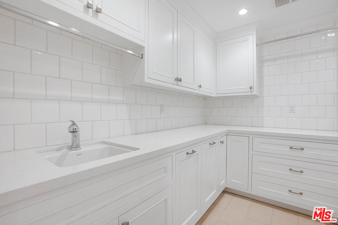 White laundry room with built-in cabinets, a long counter, and an integrated sink.