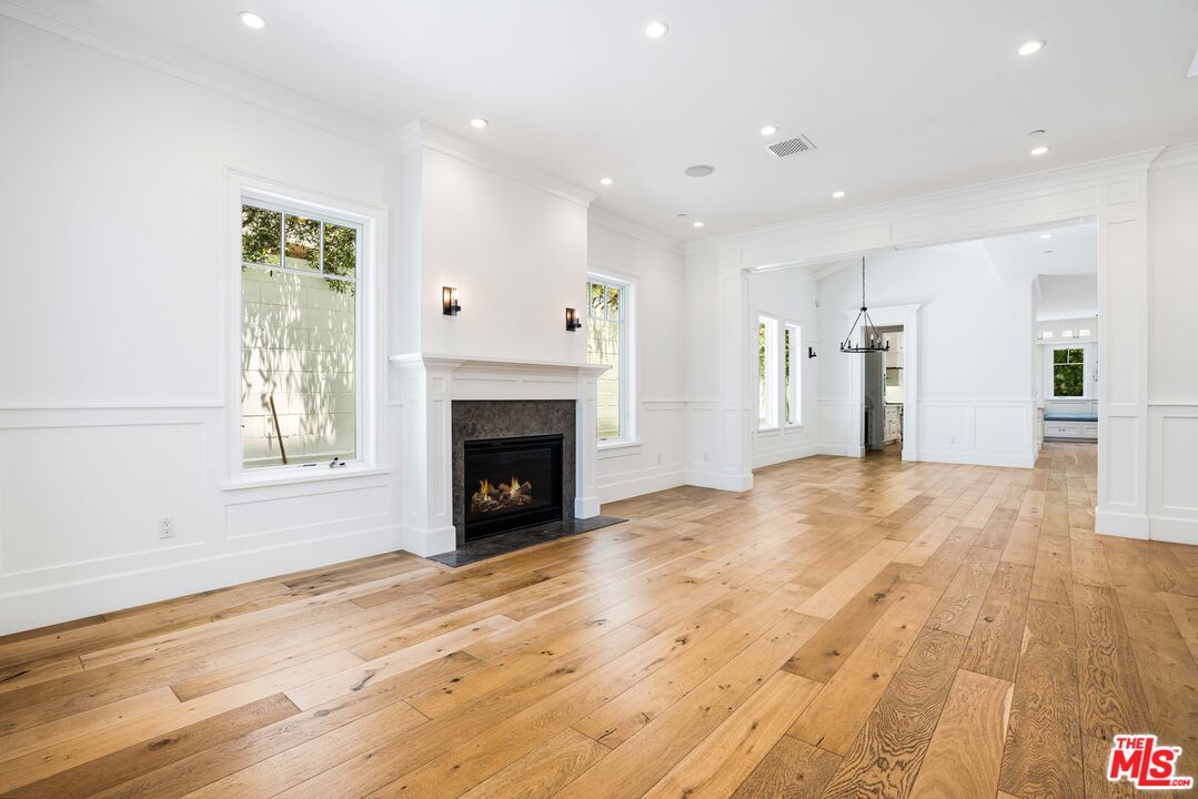 Vacant living room with a black fireplace, tall windows, and wide-plank wood floors.