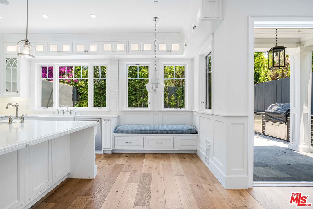 White kitchen with marble island, built-in window seat, and wide windows overlooking greenery.