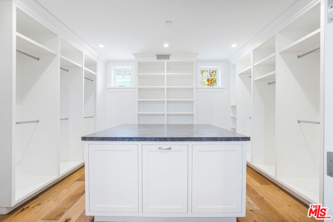 Walk-in closet with a central storage island, white built-ins, and hardwood floors.