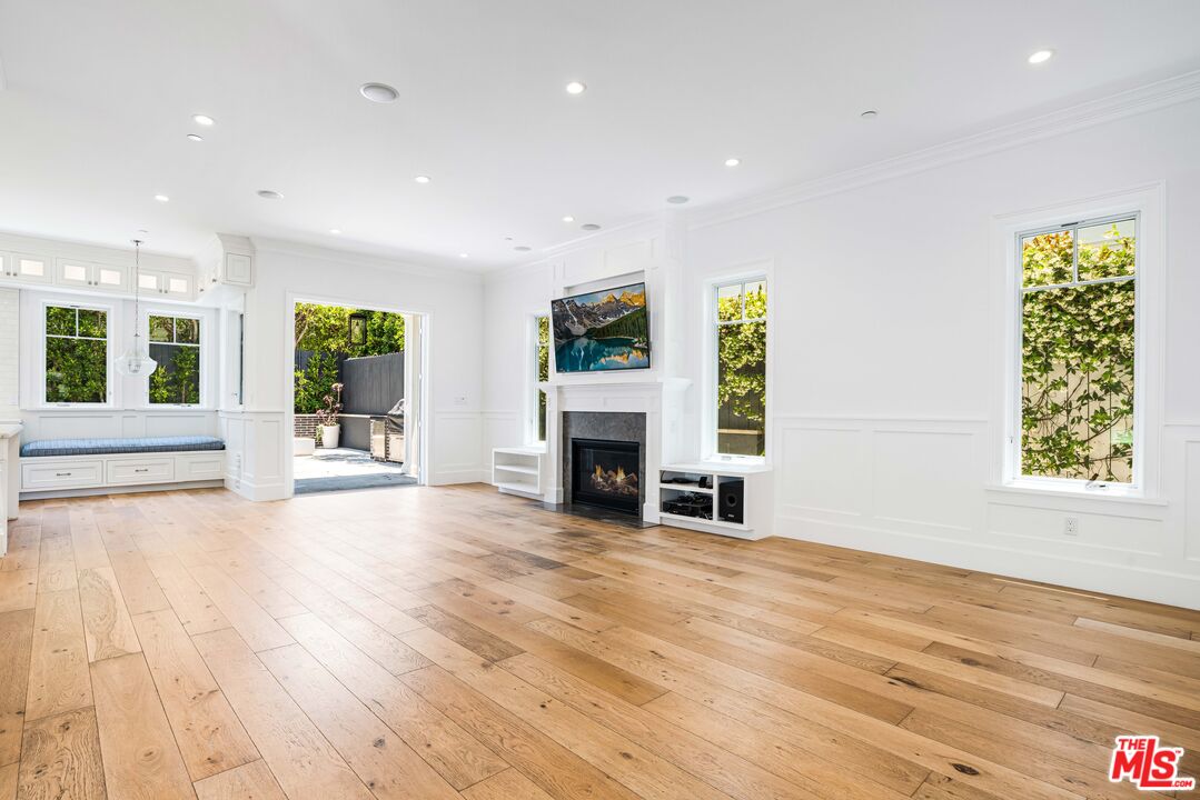 Unfurnished living room with wide-plank wood floors, fireplace, built-in window seat, and garden views.