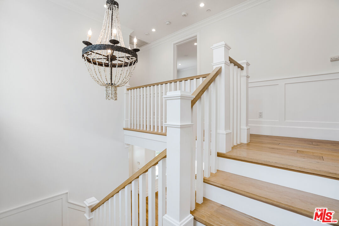 White staircase with natural wood treads, paneled walls, and a large crystal chandelier.