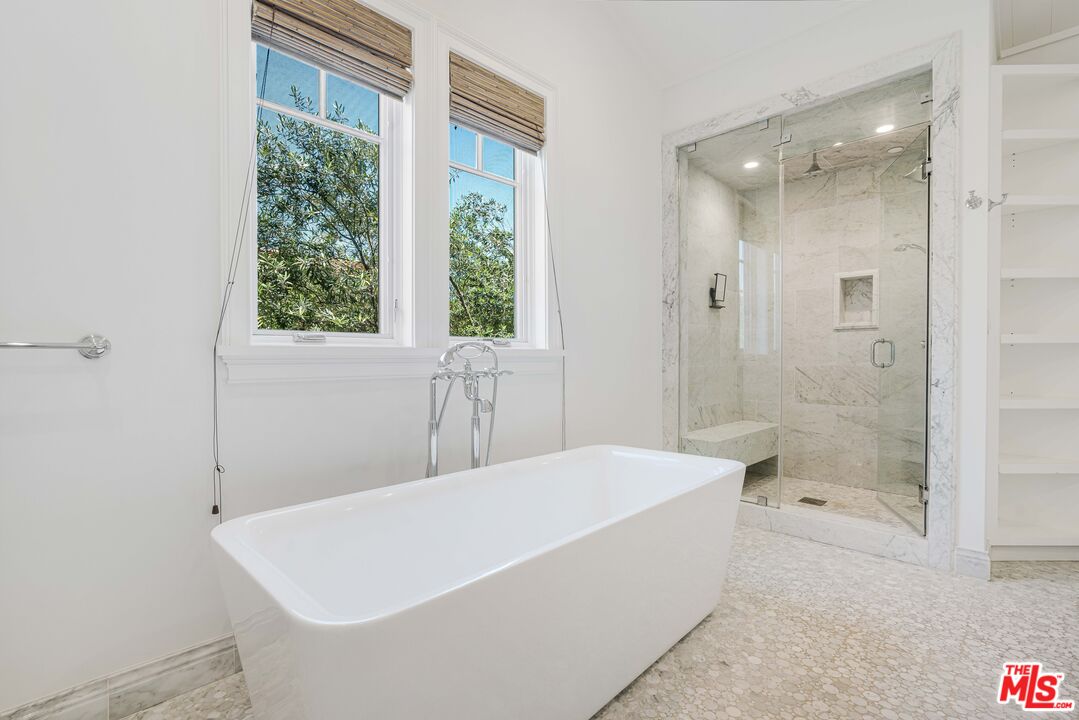 Bathroom with a freestanding soaking tub, marble walk-in shower, and windows overlooking trees.