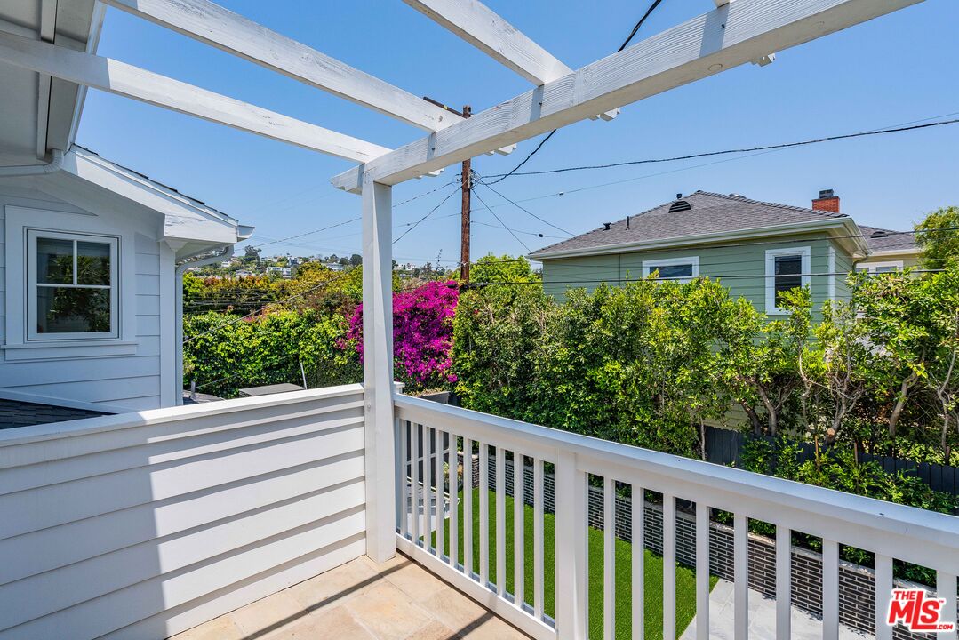 Deck with white pergola and railing overlooking a leafy garden and neighboring homes.