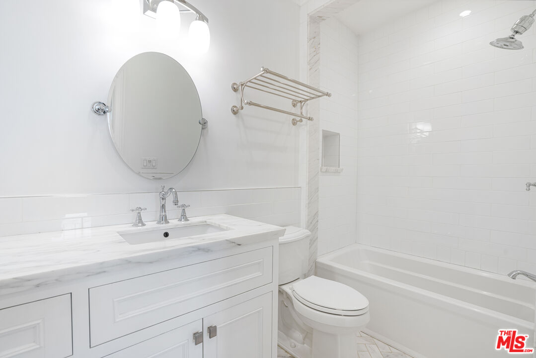 White bathroom with marble vanity, oval mirror, and tub-shower.
